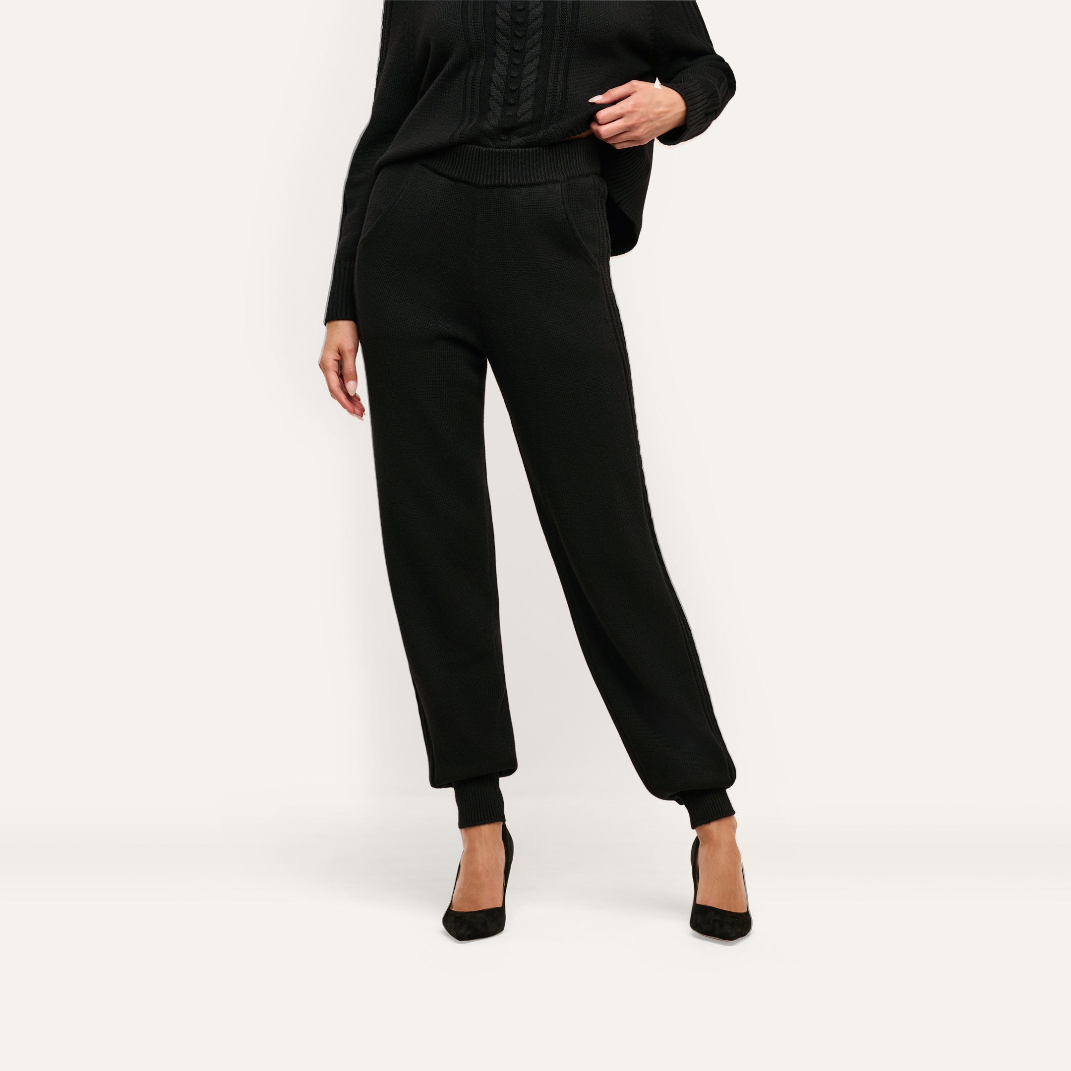 Black Tamaris Cable Knit Pant featuring a high, ribbed elastic waistband and cuffed ankles, styled as a slim-fit jogger with black pointed-toe heels.