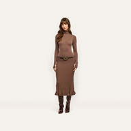 A person wearing a brown, lightweight Solaire Knit Dress featuring a funnelneck, long sleeves, a wide belt with an ornate buckle, and knee-high boots.