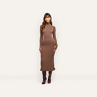 A woman wearing the Solaire Knit Dress in a brown funnelneck midi style with thumbhole sleeves, paired with dark brown knee-high boots.