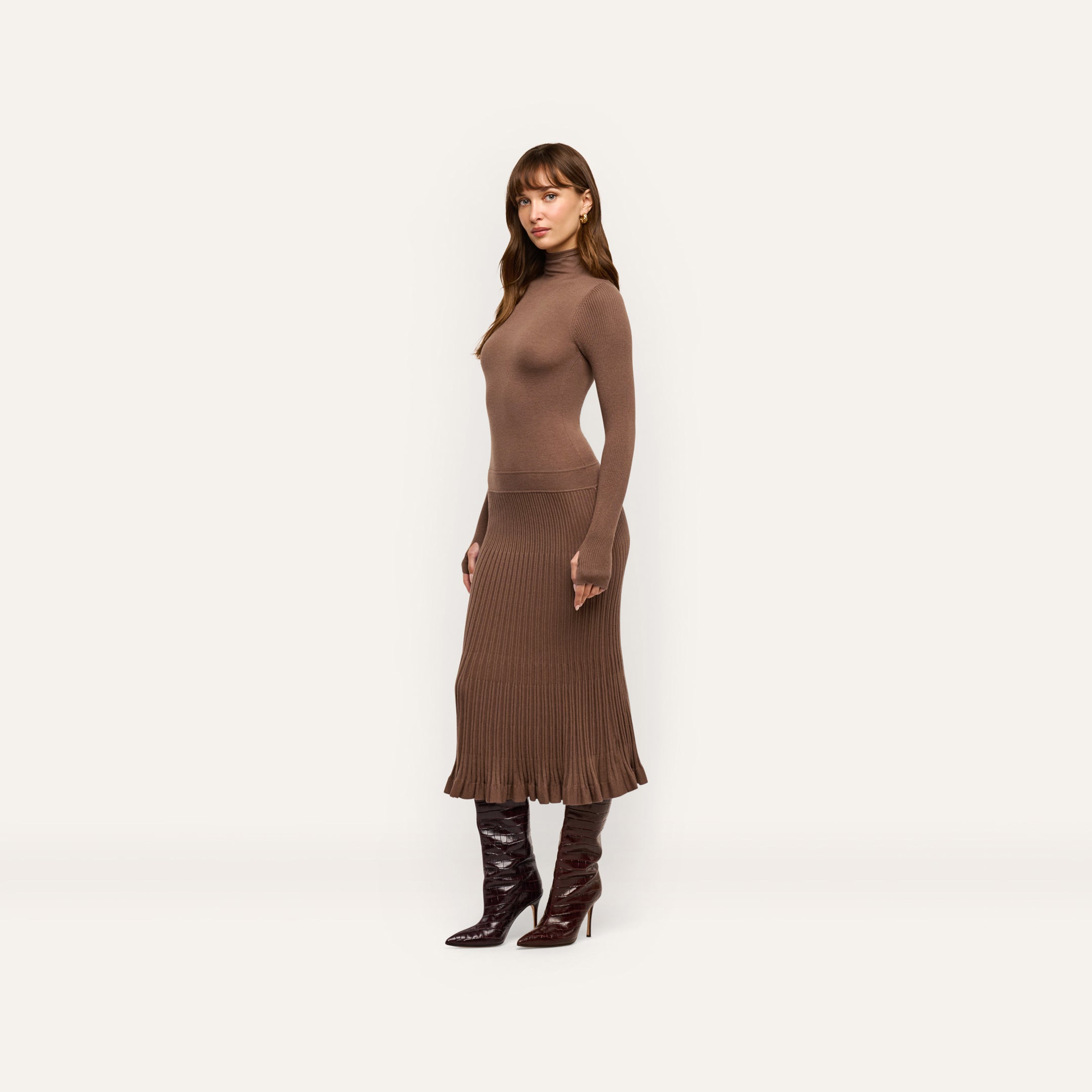 A woman models the brown Solaire Knit Dress, a long-sleeve lightweight midi dress featuring a funnelneck and ribbed skirt, paired with dark knee-high boots.