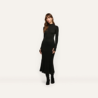 A woman wearing a Solaire Knit Dress, a fitted black long-sleeved mock-neck midi dress with a ribbed skirt, paired with black knee-high boots.