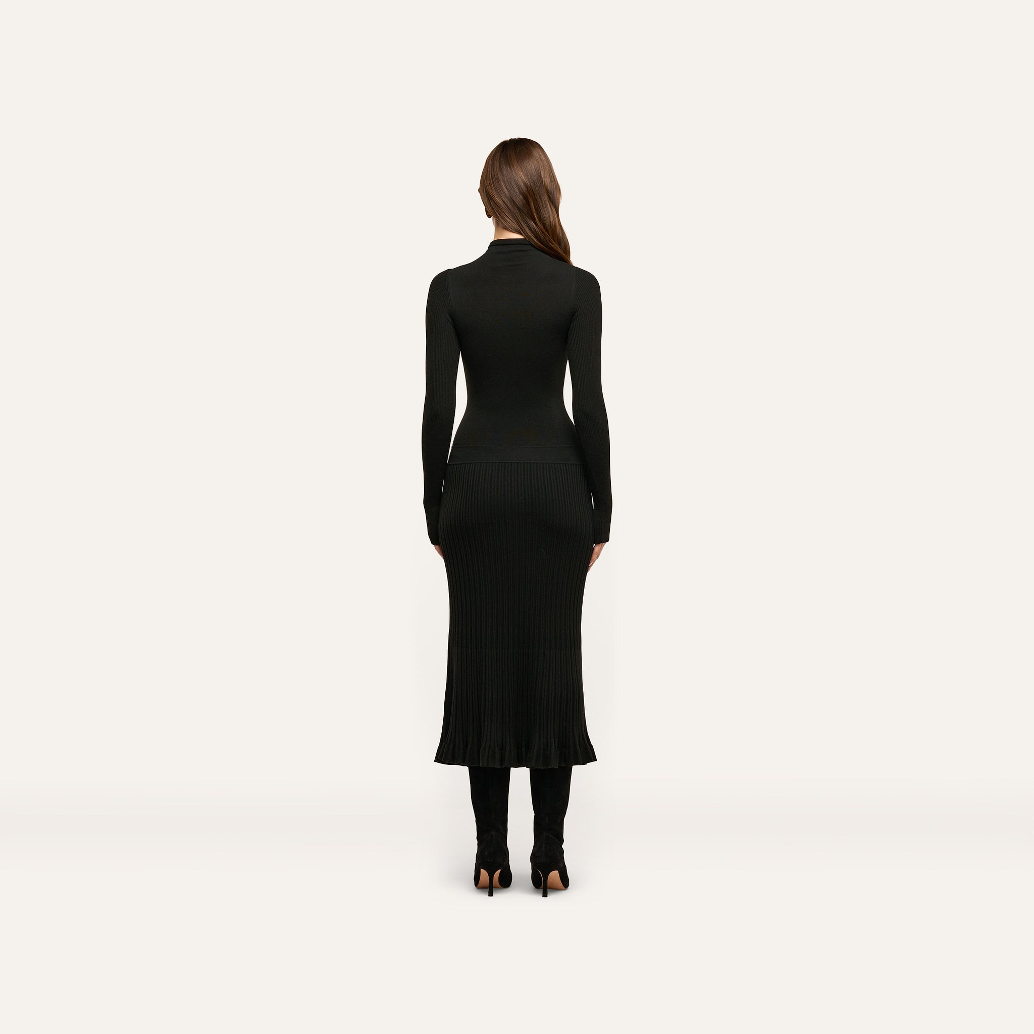 A woman seen from behind wearing a black long-sleeved mock-neck fitted Solaire Knit Dress with a ribbed skirt and black heeled boots.