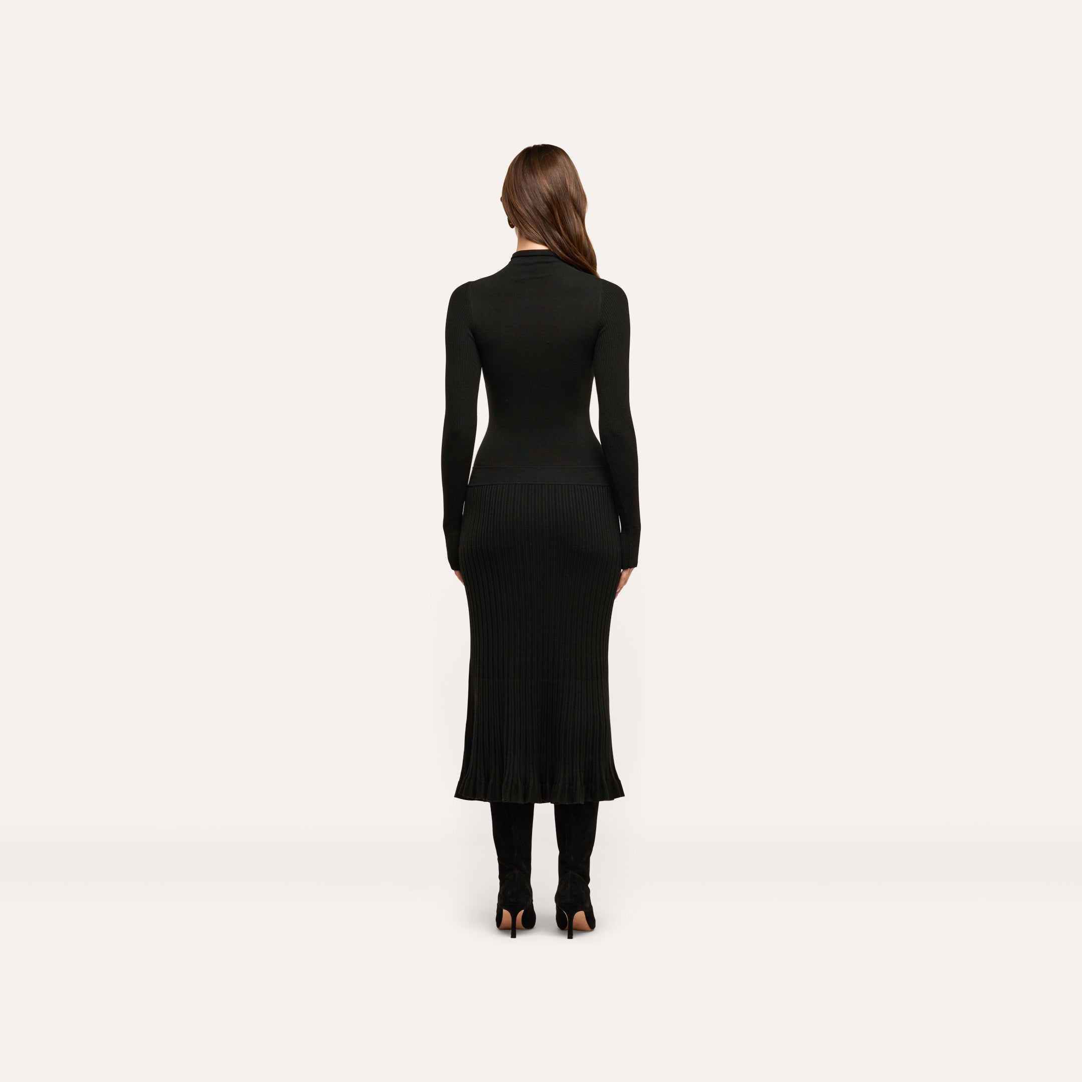 A woman seen from behind wearing a black long-sleeved mock-neck fitted Solaire Knit Dress with a ribbed skirt and black heeled boots.