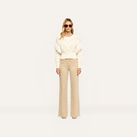 Woman wearing an Ottavia Pullover in cream-colored cable knit with fringe trim on the sleeves, paired with wide-leg tan trousers.