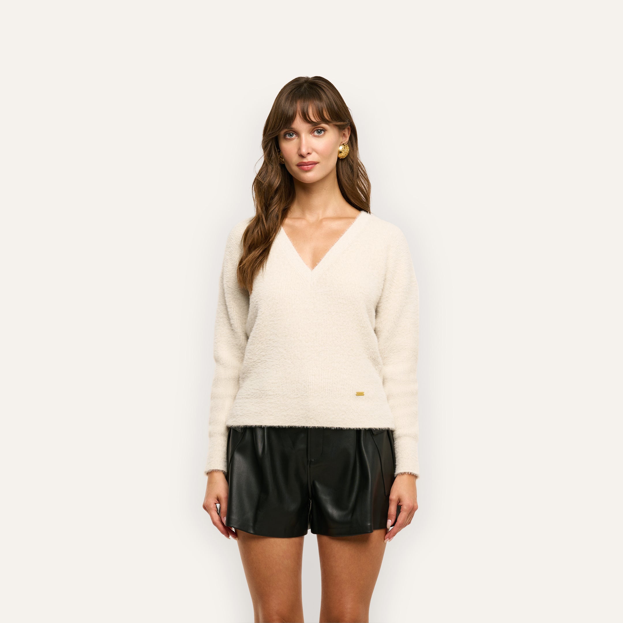 A woman wearing a cream Korinna Pullover V-neck sweater and black shorts.