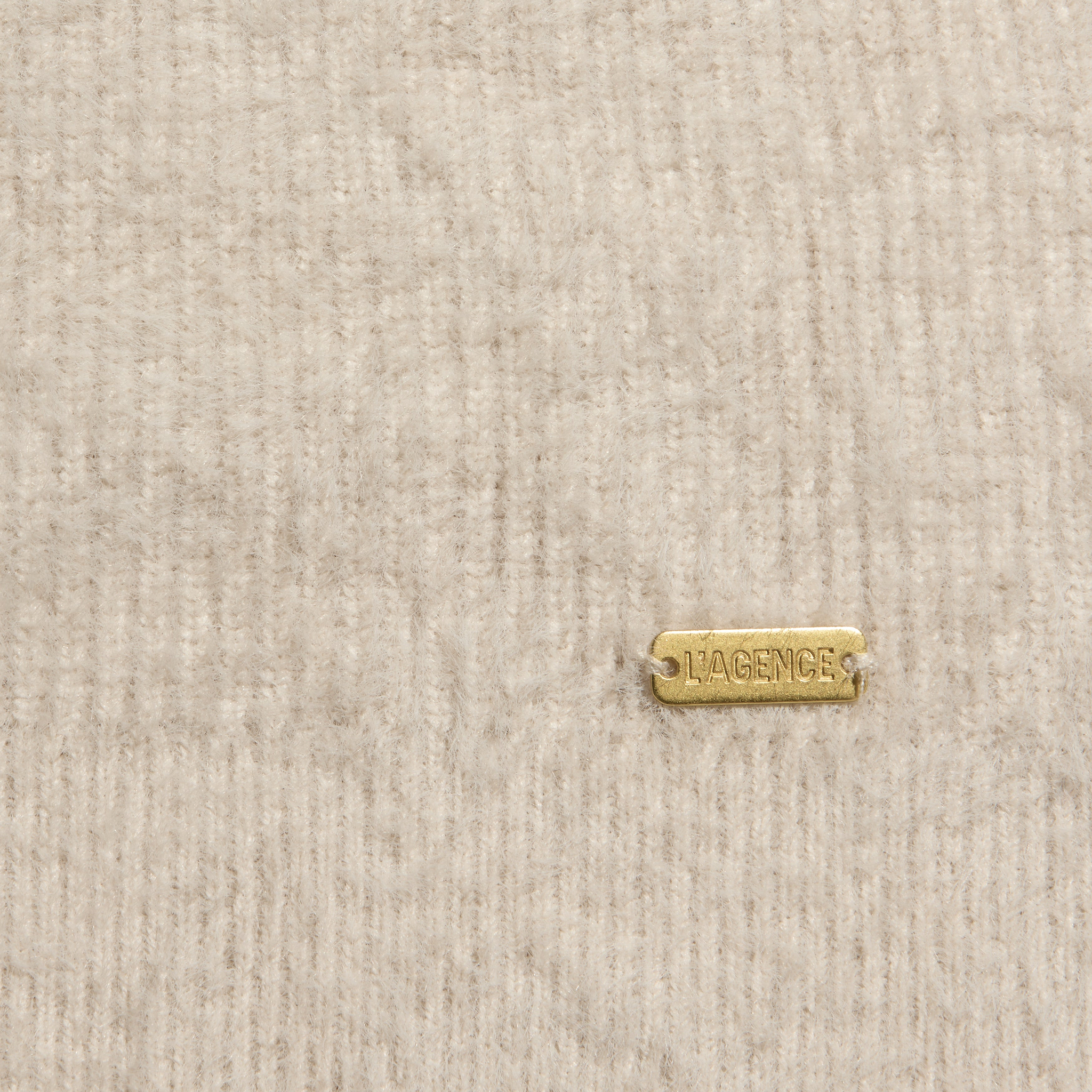 Close-up of a fuzzy, ribbed beige Korinna Pullover featuring a small rectangular gold-tone metal tag engraved with LAGENCE.