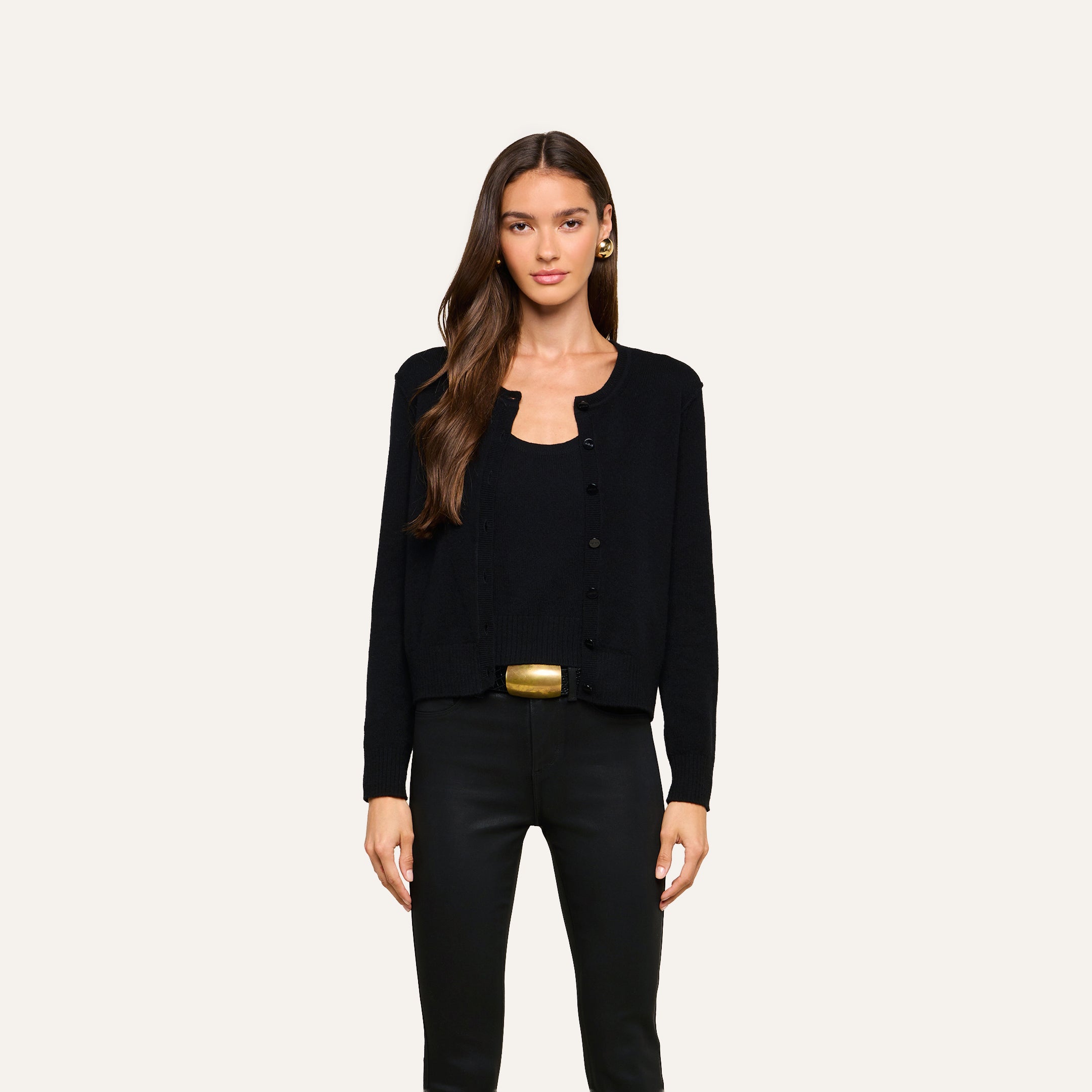 A woman with long brown hair wears the Malone Cashmere Cardigan in black over a matching top and black pants, standing against a plain light background.