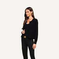 Wearing the Malone Cashmere Cardigan in black over a matching top and pants, a woman with long brown hair stands against a plain light background, accessorized with a black belt and gold earrings.