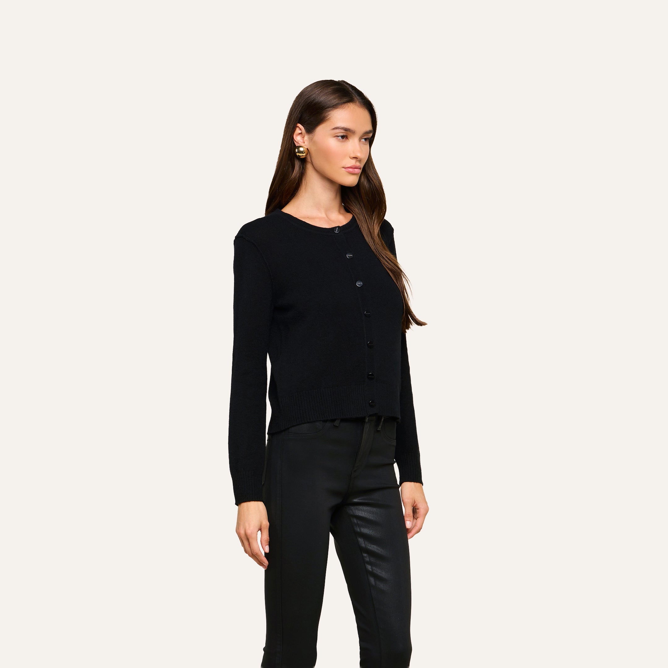 A woman with long brown hair, wearing the Malone Cashmere Cardigan in black and black pants, stands against a plain light background, facing slightly to the right with a neutral expression.