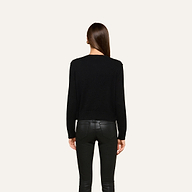 A person with straight brown hair, seen from behind, wears the Malone Cashmere Cardigan and black leather pants, standing against a plain light background.