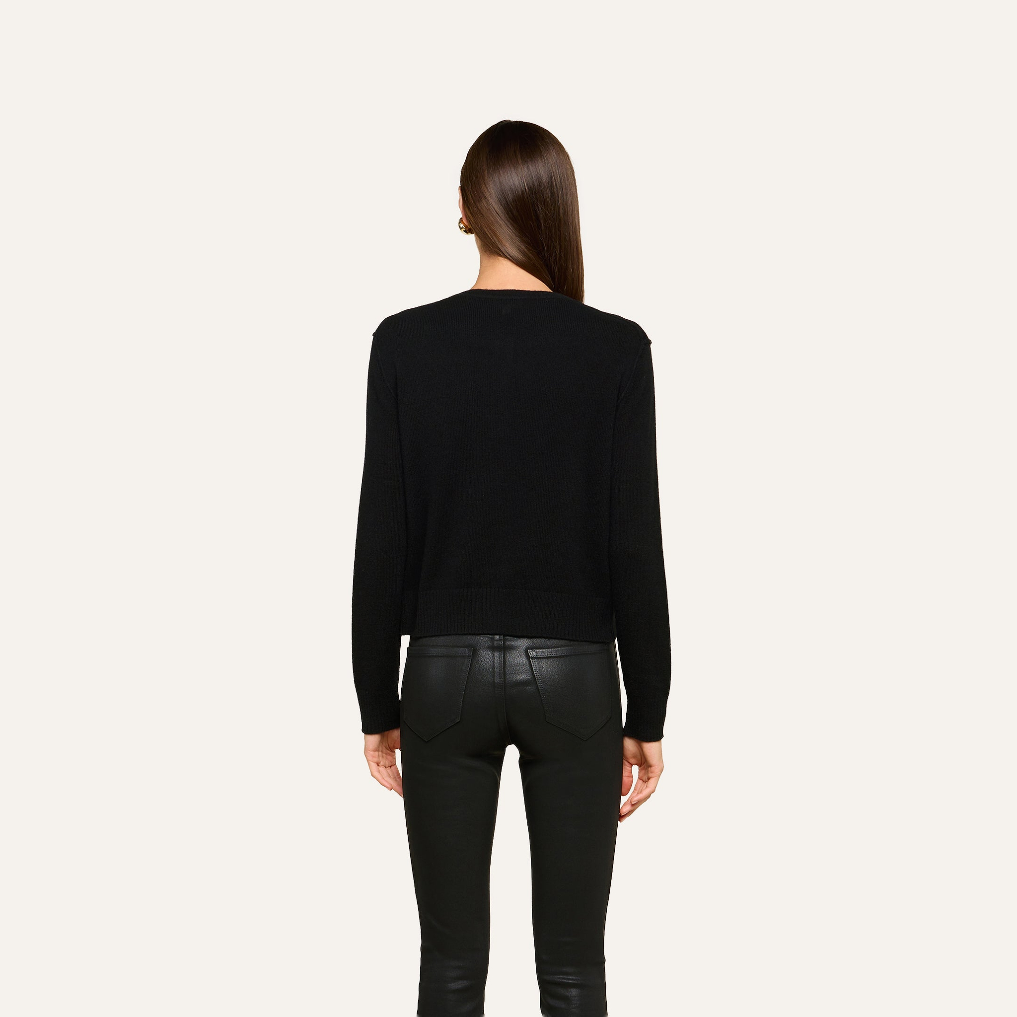 A person with straight brown hair, seen from behind, wears the Malone Cashmere Cardigan and black leather pants, standing against a plain light background.