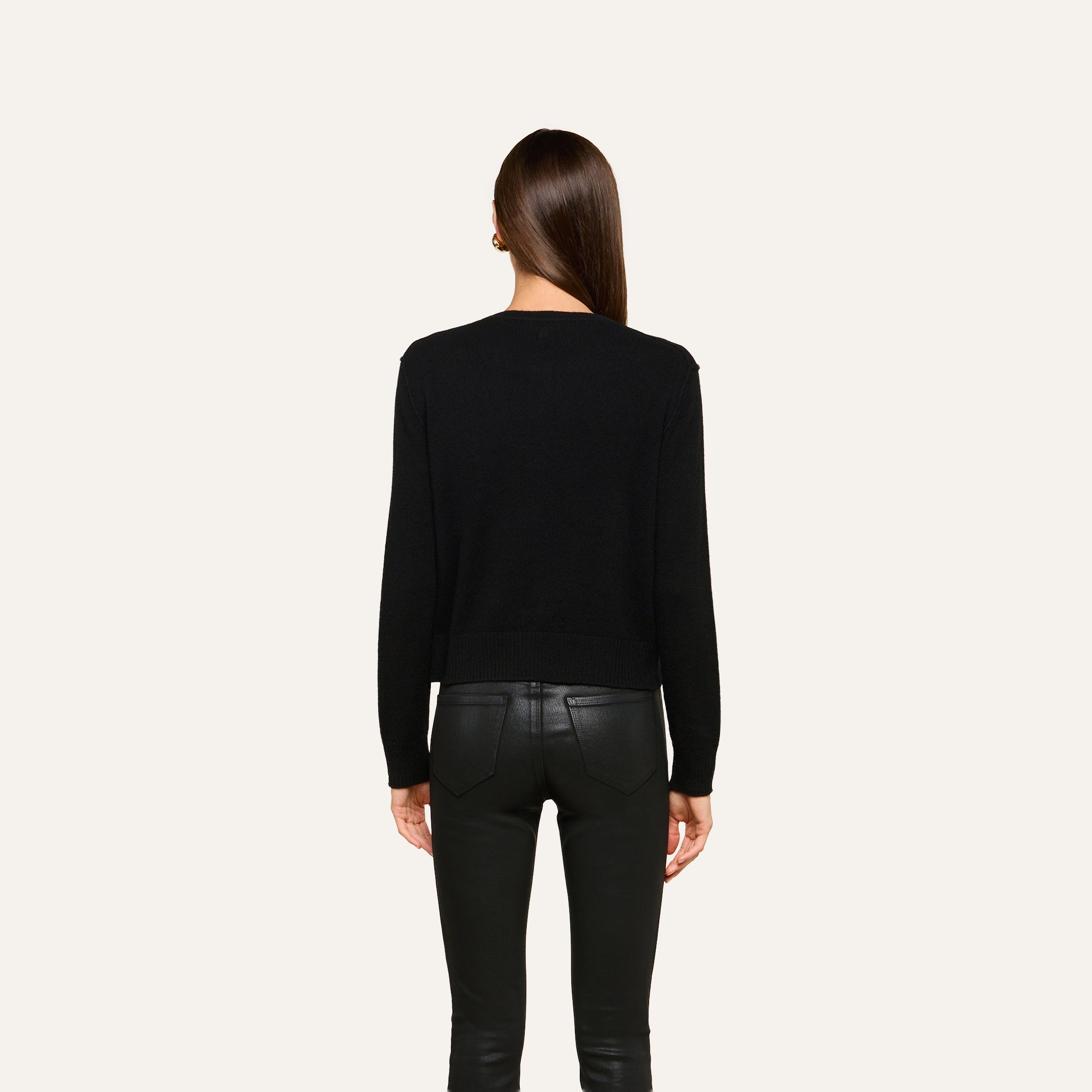 A person with straight brown hair, seen from behind, wears the Malone Cashmere Cardigan and black leather pants, standing against a plain light background.