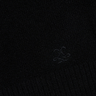 A close-up of the black textured fabric from the Malone Cashmere Cardigan, featuring a subtle embroidered logo or symbol near the bottom center.