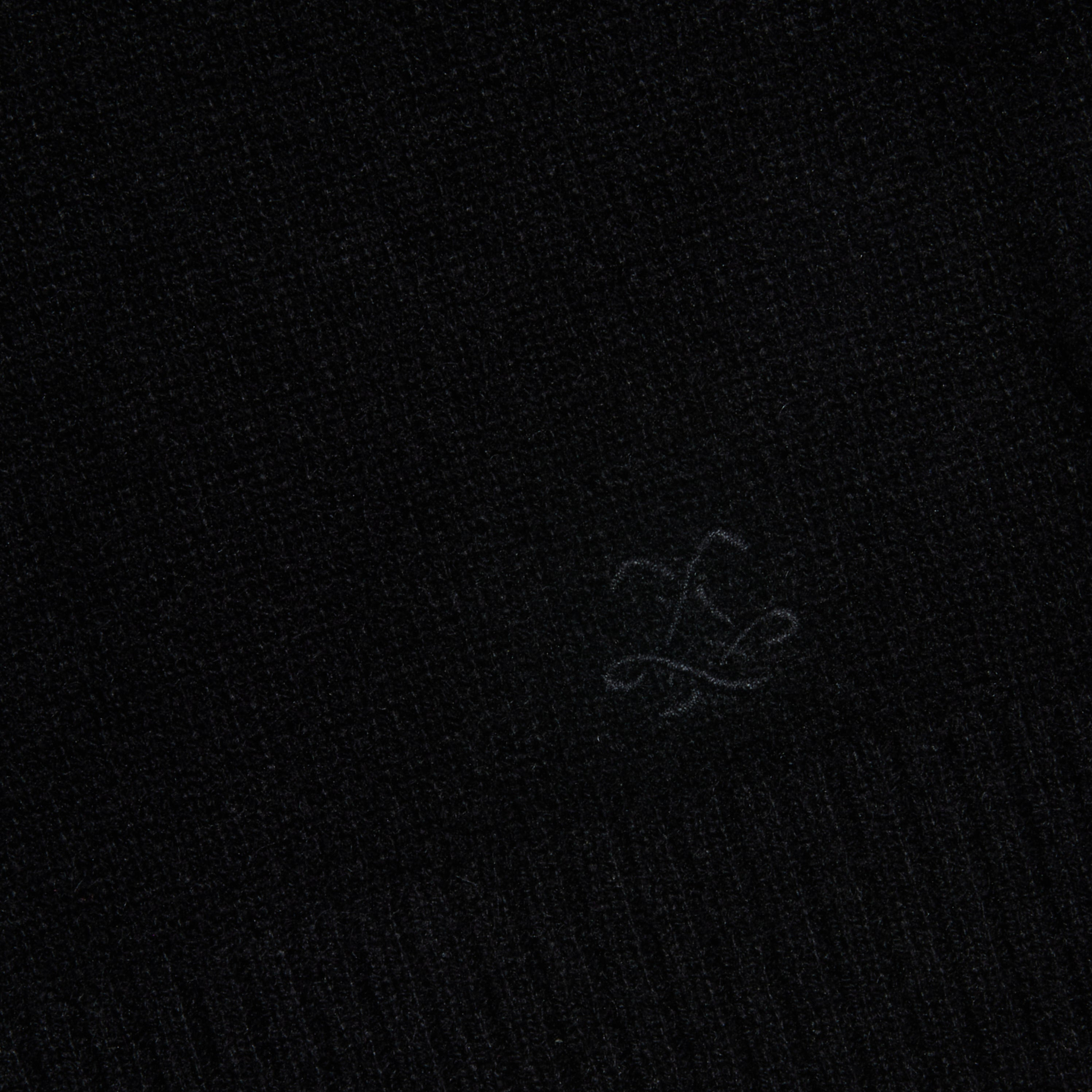 A close-up of the black textured fabric from the Malone Cashmere Cardigan, featuring a subtle embroidered logo or symbol near the bottom center.