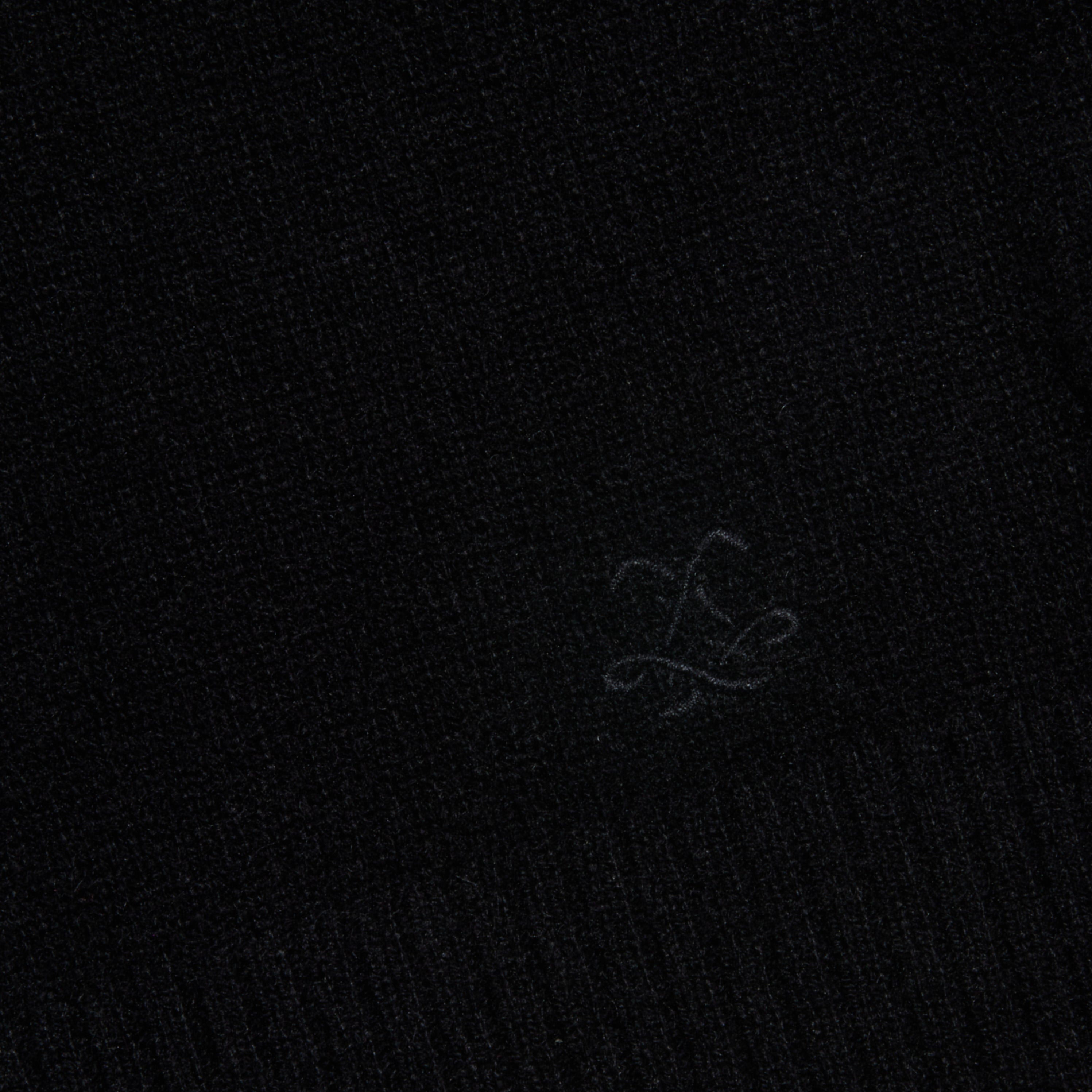 A close-up of the black textured fabric from the Malone Cashmere Cardigan, featuring a subtle embroidered logo or symbol near the bottom center.