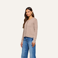 A woman wearing the Malone Cashmere Cardigan and blue jeans stands against a plain off-white background, looking slightly to the side with a neutral expression.