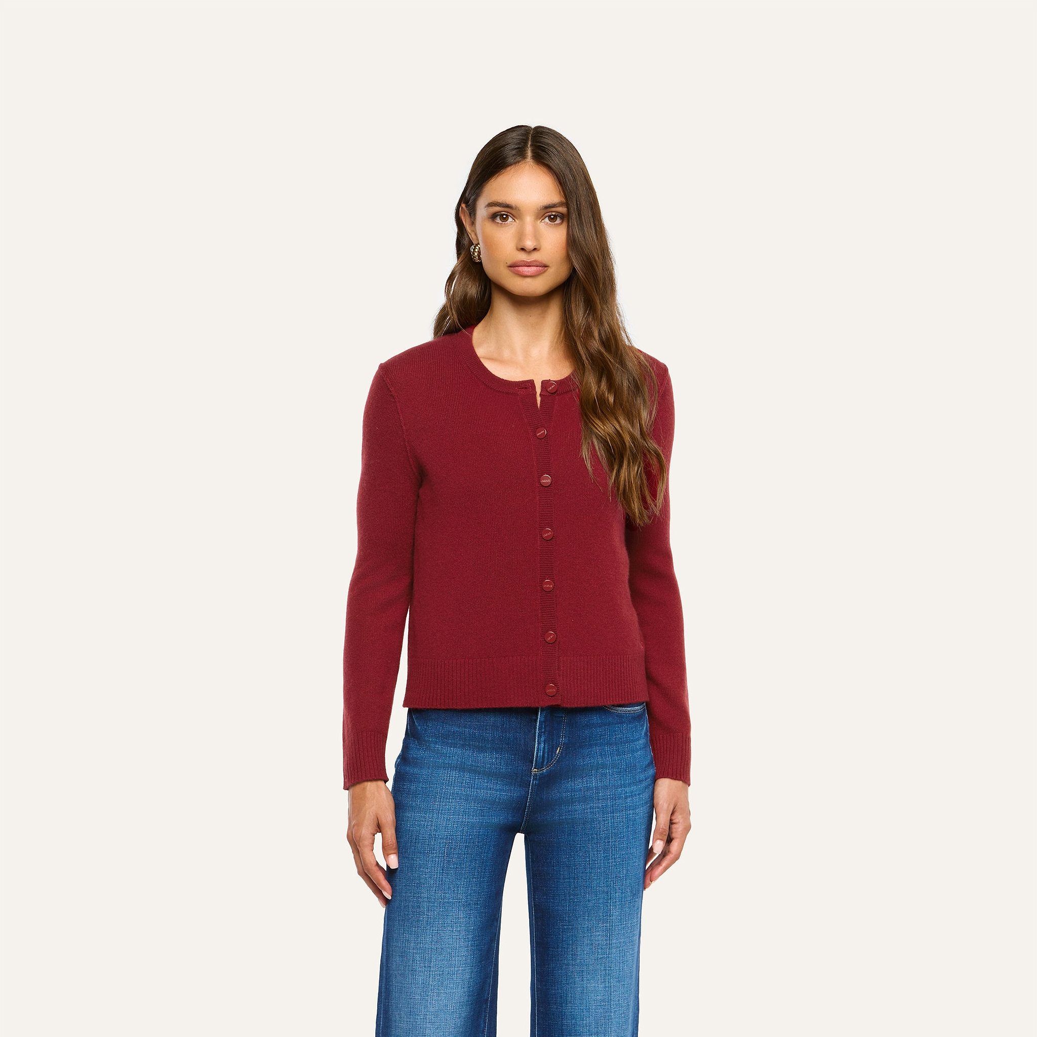 A model wears a burgundy, cherry red Malone Cashmere Cardigan with a button-front closure, paired with blue jeans.