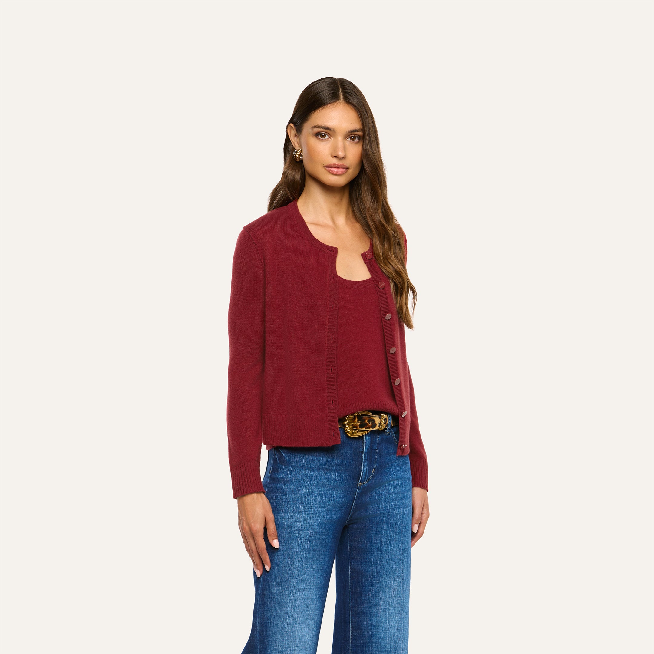 A woman wears a cherry red Malone Cashmere Cardigan and matching tank top with blue jeans and a patterned belt.