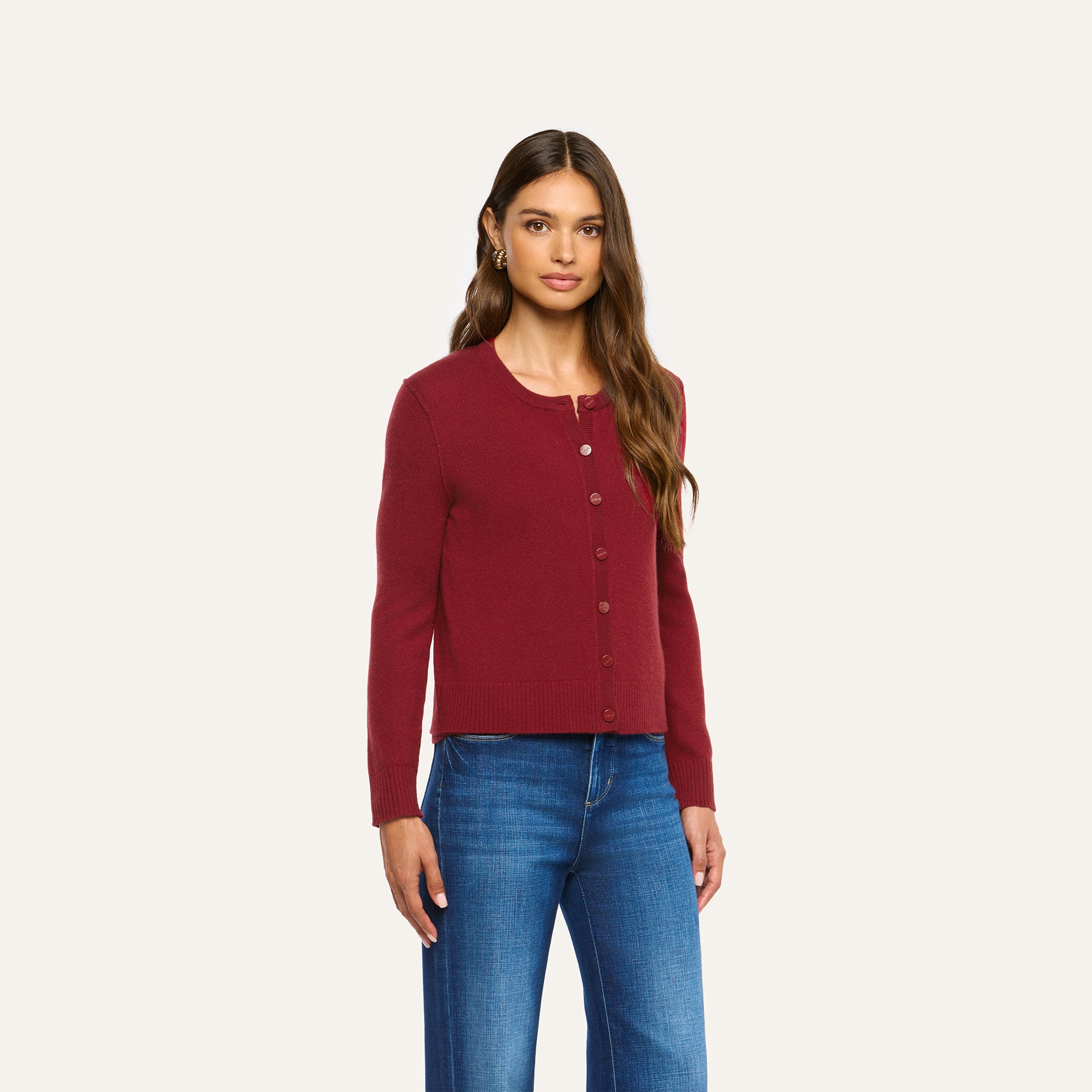 A person wearing a cherry red, long-sleeved Malone Cashmere Cardigan and blue jeans.