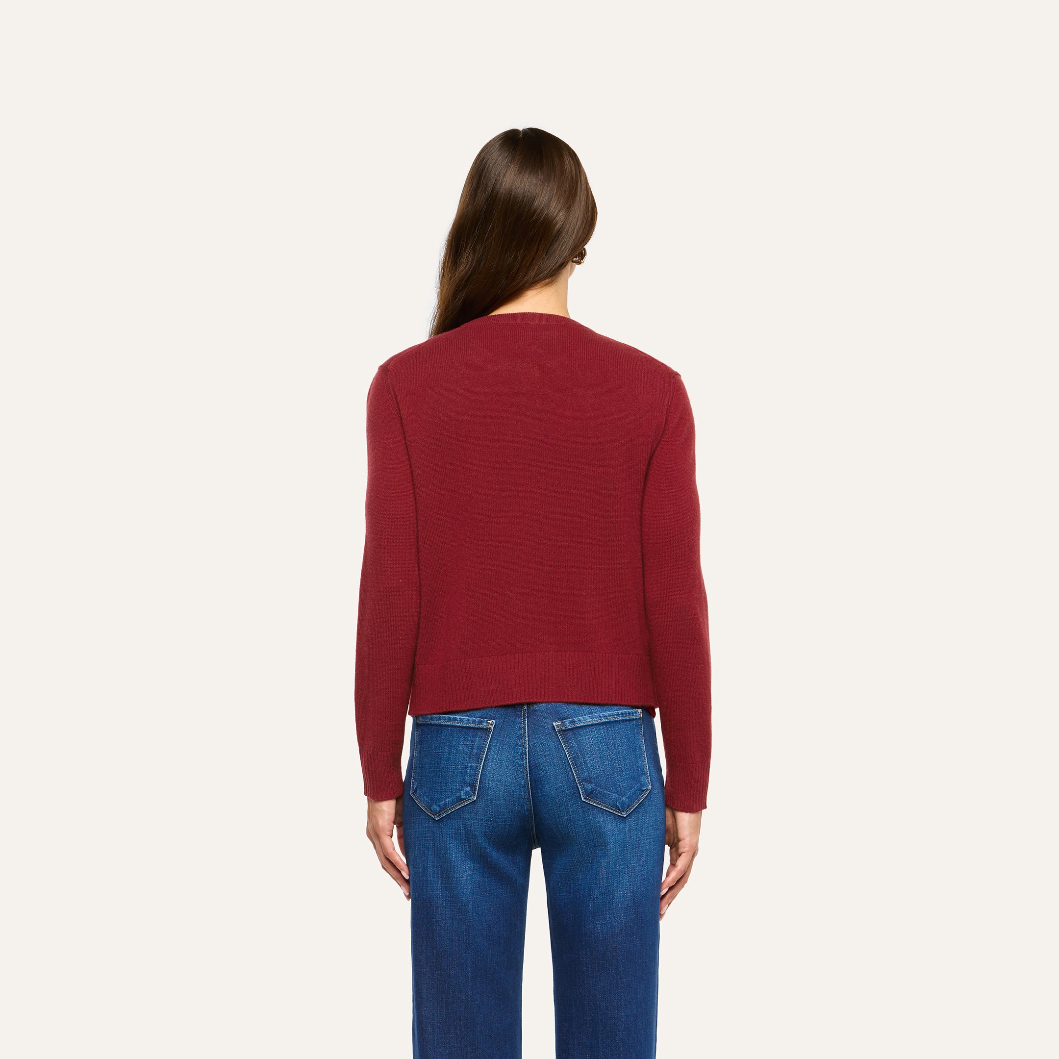 A person seen from behind, wearing a cherry red Malone Cashmere Cardigan and blue jeans.