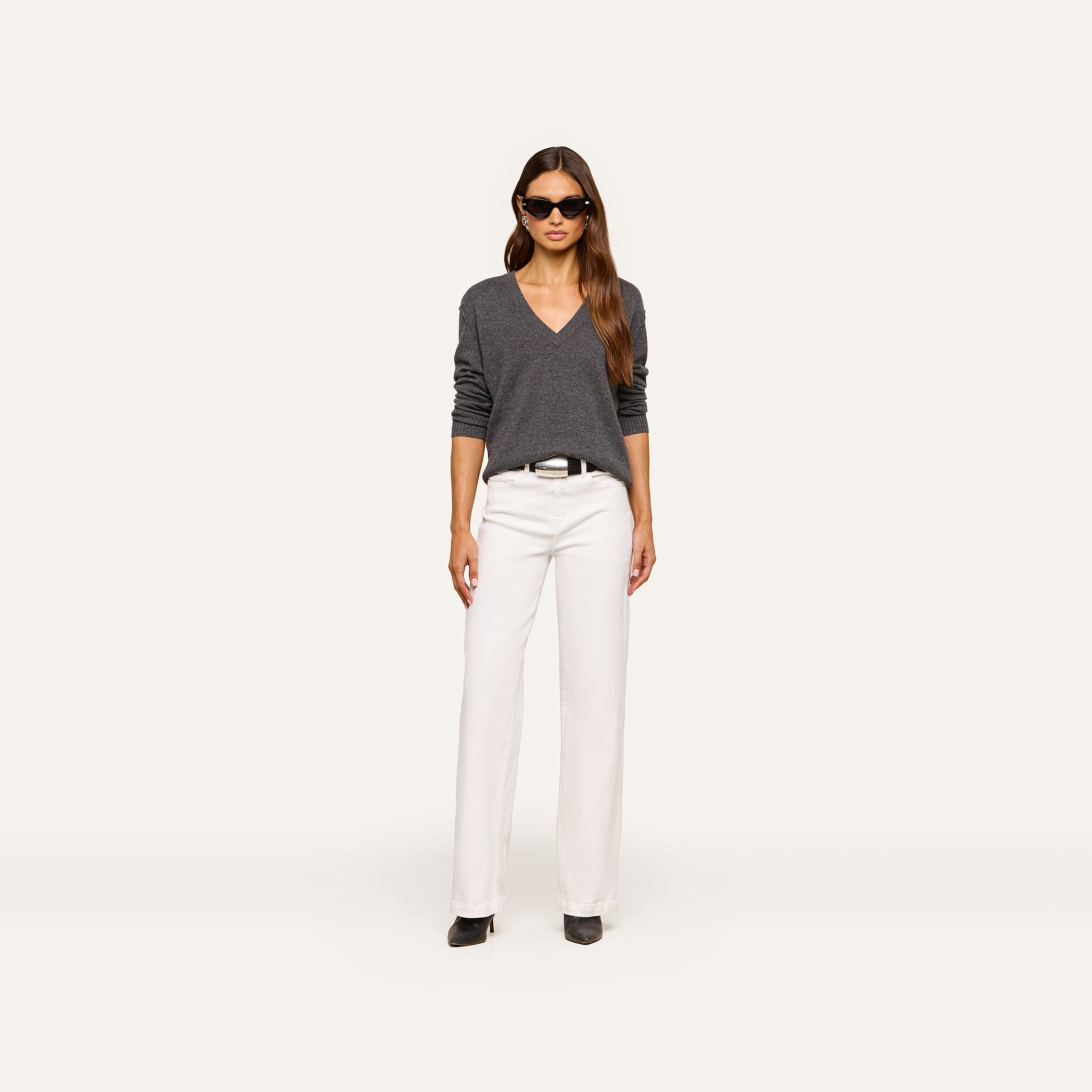 A woman wearing sunglasses, white pants, black shoes, and the Spence Cashmere Pullover stands facing forward against a plain white background.