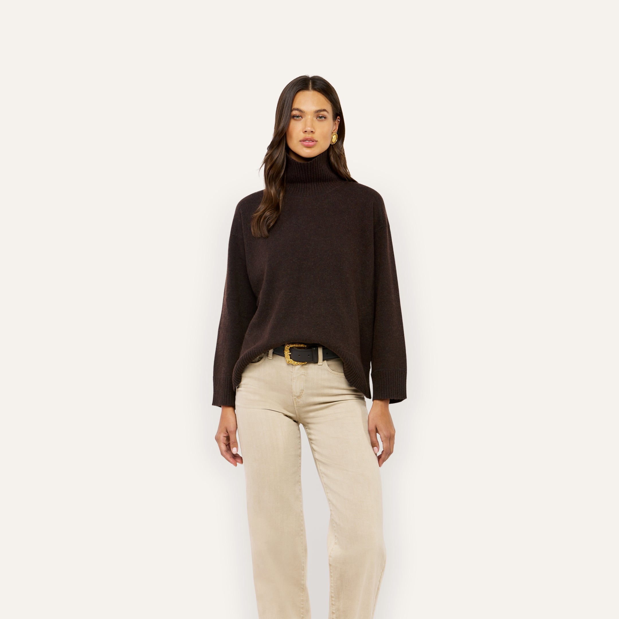 A person wearing a dark brown Selwyn Oversized Turtleneck paired with tan jeans and a black belt.