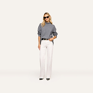 A woman wearing sunglasses, the Selwyn Oversized Turtleneck in heather grey wool cotton, white wide-leg pants, and black shoes stands against a plain, light background with one hand in her pocket.