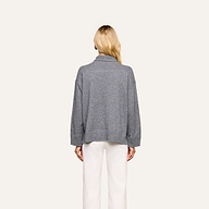 A person with long blonde hair, seen from behind, wears the Selwyn Oversized Turtleneck in heather grey paired with white pants, standing against a plain light background.
