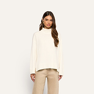 A person wearing a cream-colored merino wool Selwyn Oversized Turtleneck and tan pants.