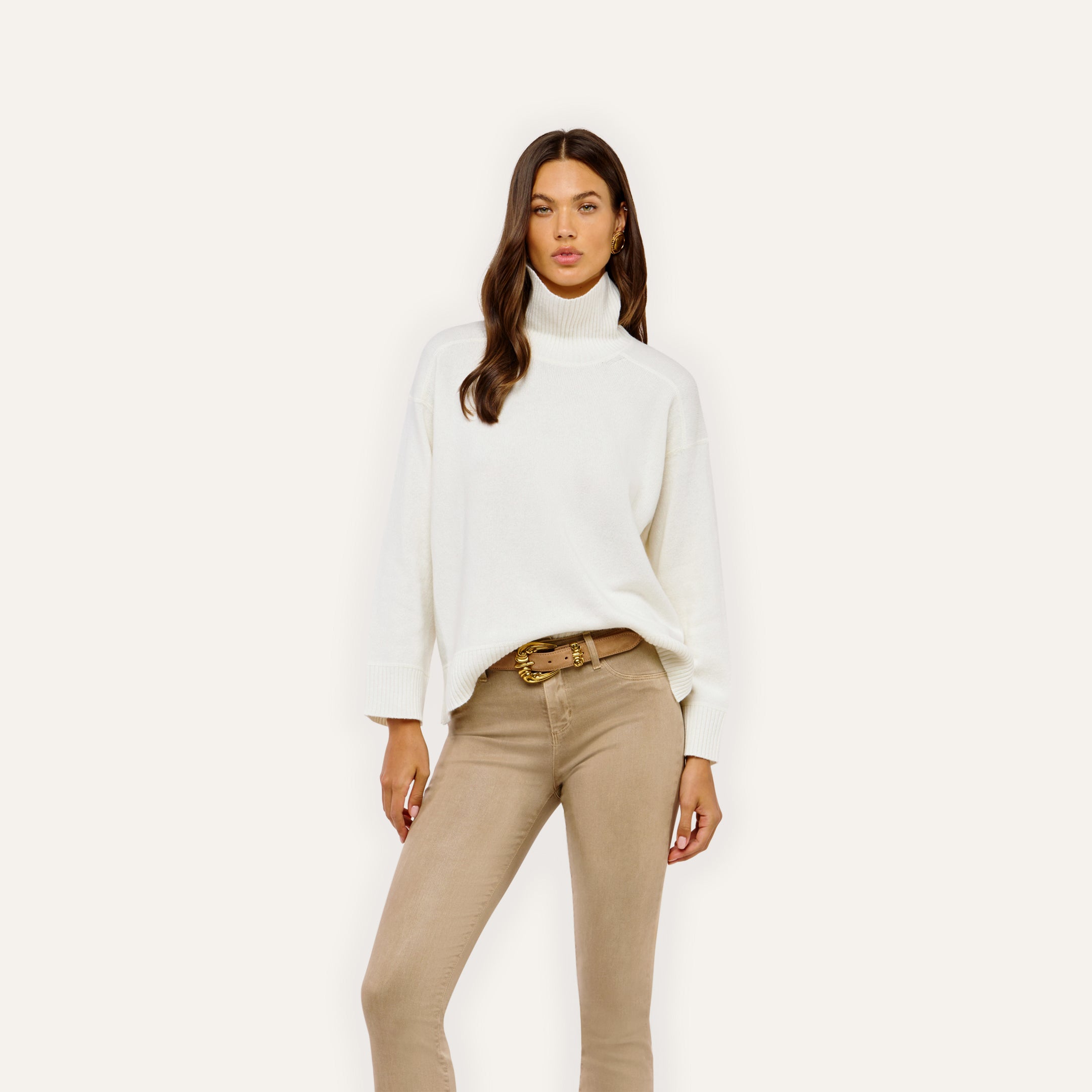 A person wearing a Selwyn Oversized Turtleneck in merino wool with tan jeans and a light brown belt.