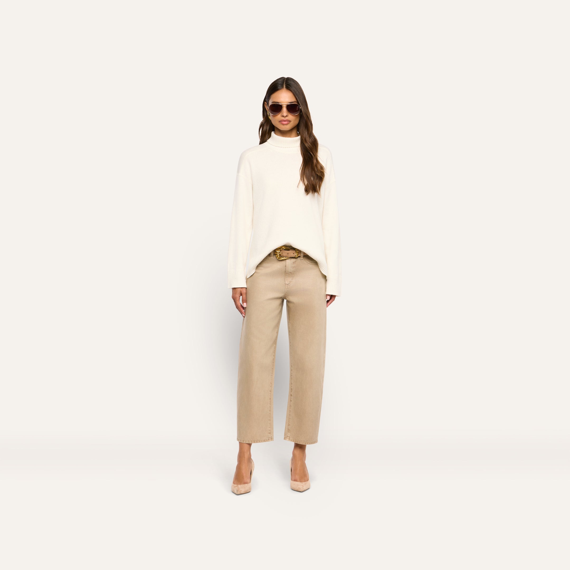 Woman wearing a Selwyn Oversized Turtleneck merino wool sweater, tan jeans with a belt, and tan pumps.