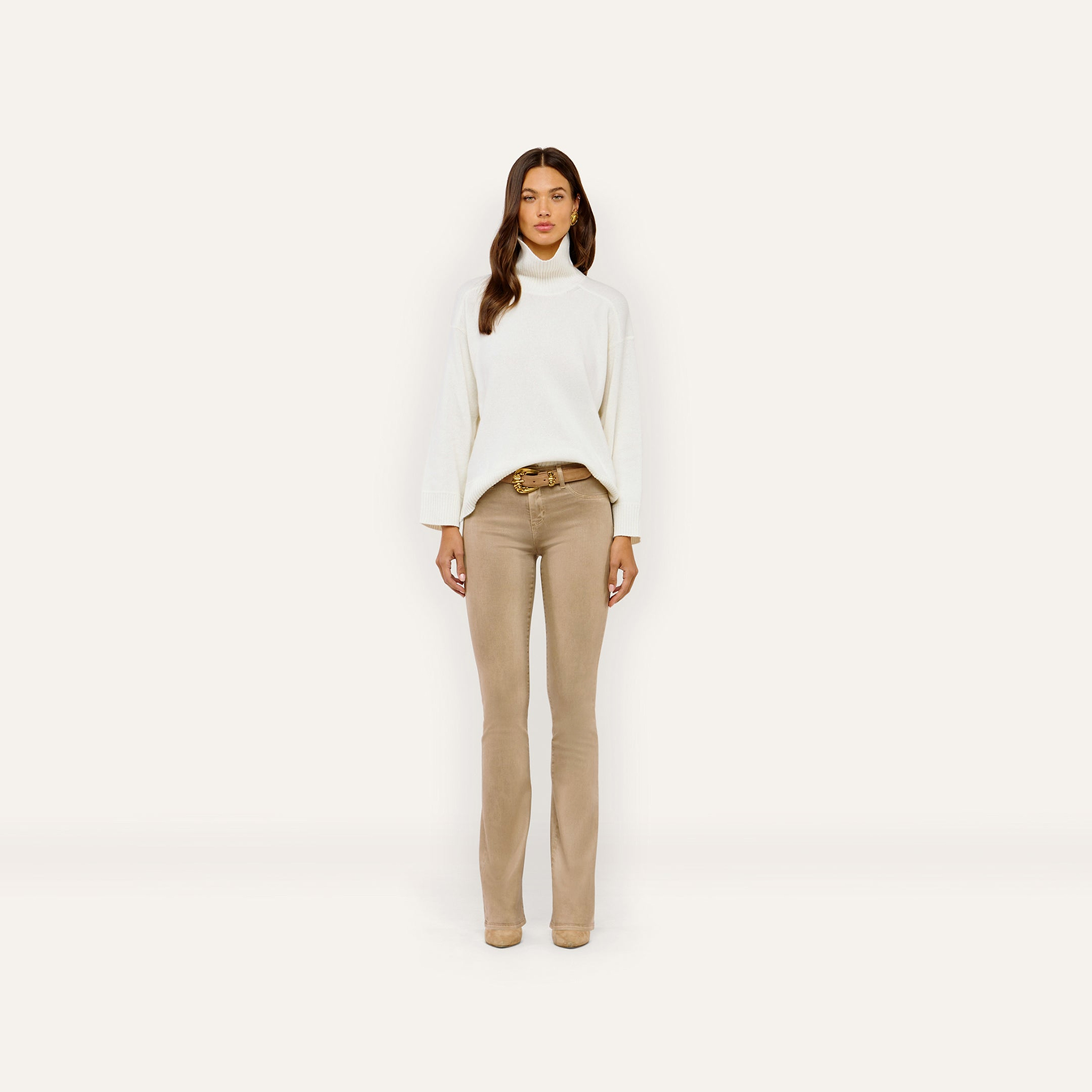 A person wearing a white Selwyn Oversized Turtleneck tucked into tan trousers with a gold-buckled belt.