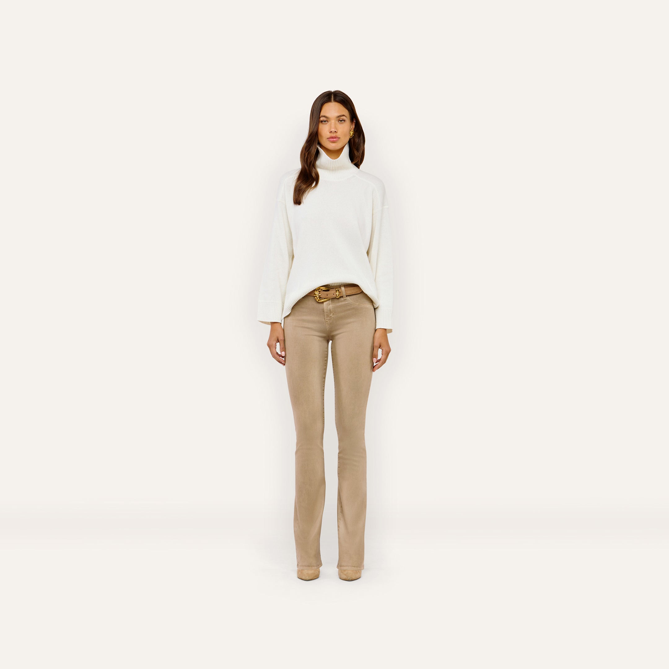 A person wearing a white Selwyn Oversized Turtleneck tucked into tan trousers with a gold-buckled belt.