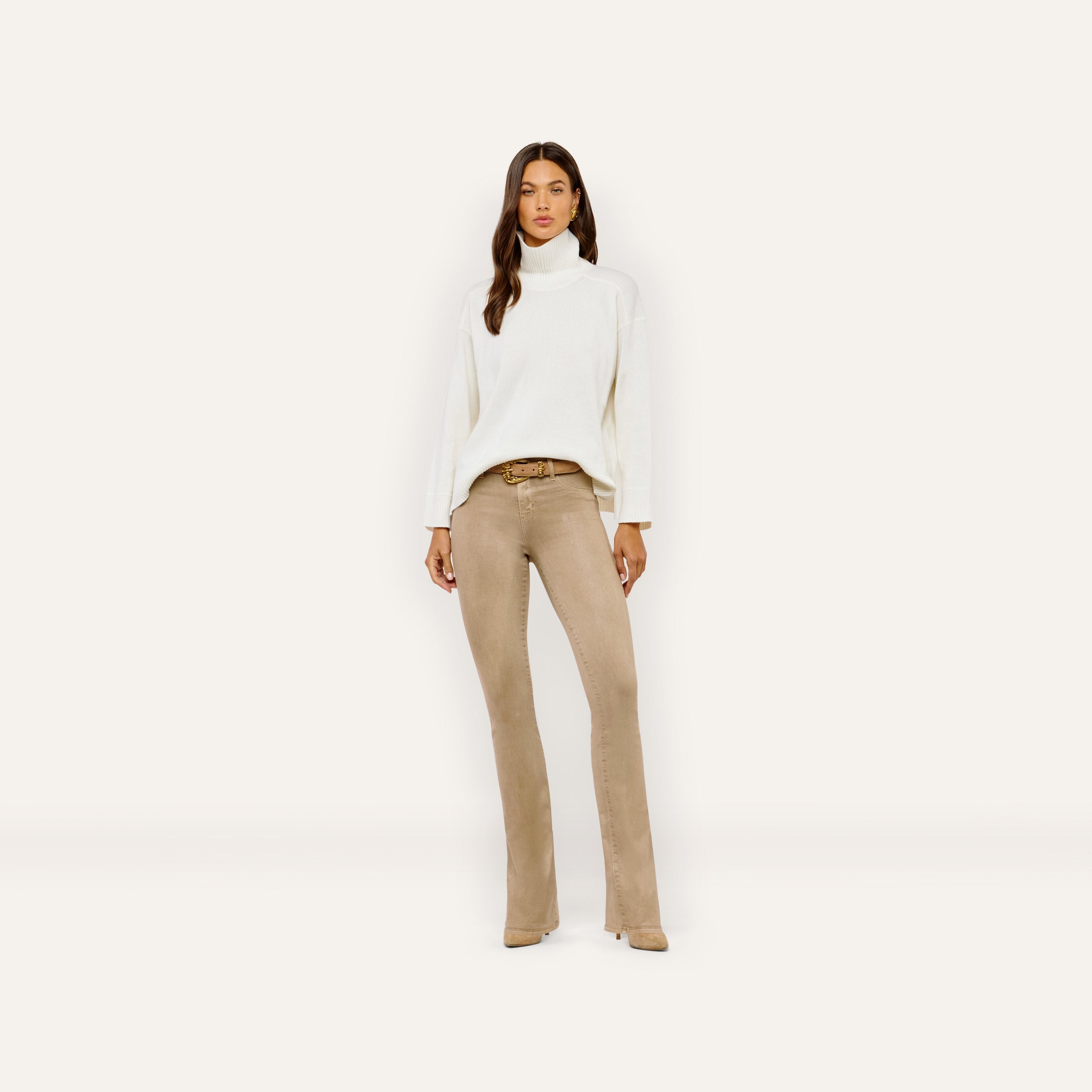 A person wears an oversized merino wool Selwyn Oversized Turtleneck with tan flared jeans and a gold-buckled belt.