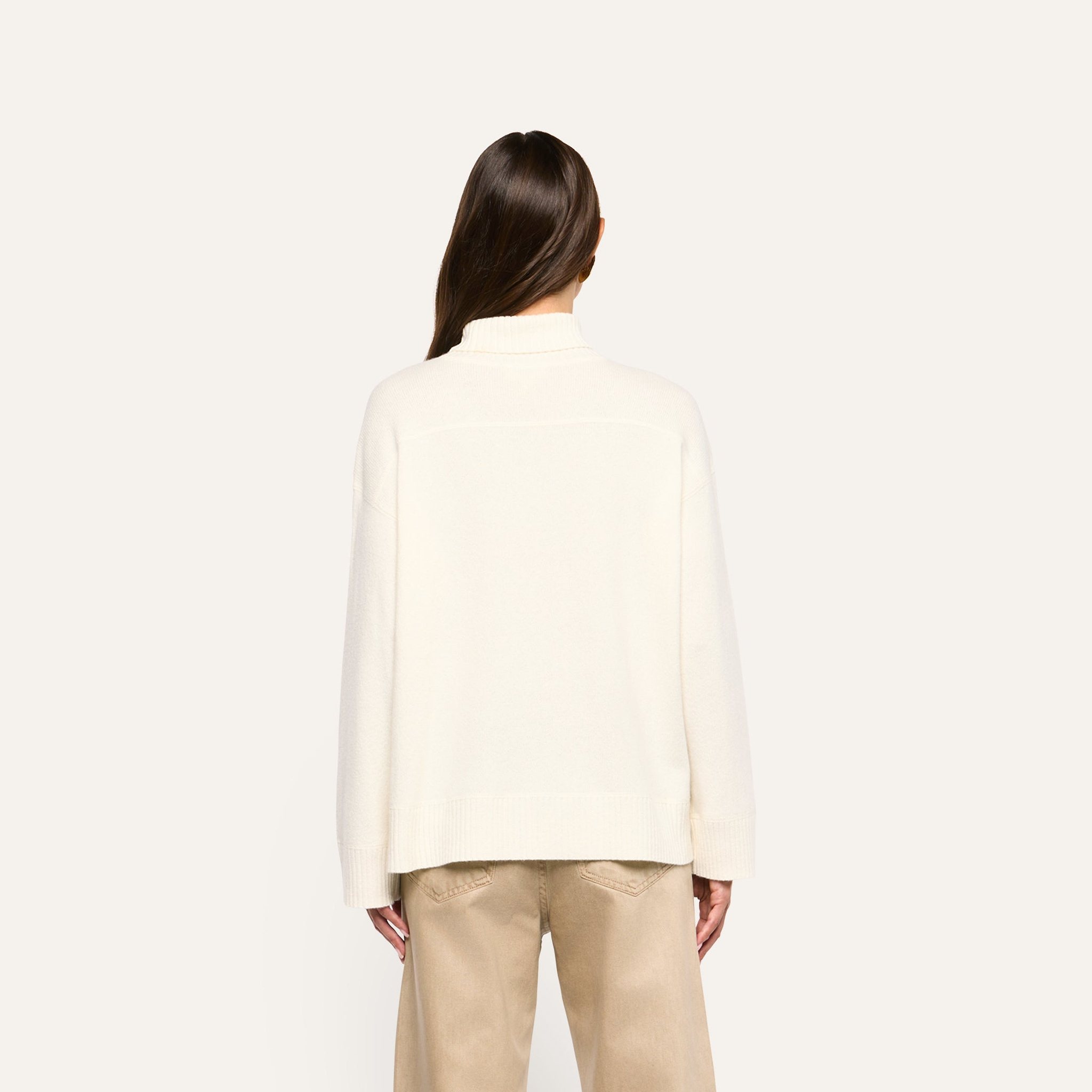 Back view of a person wearing a cream-colored oversized Selwyn Oversized Turtleneck in merino wool and tan pants.