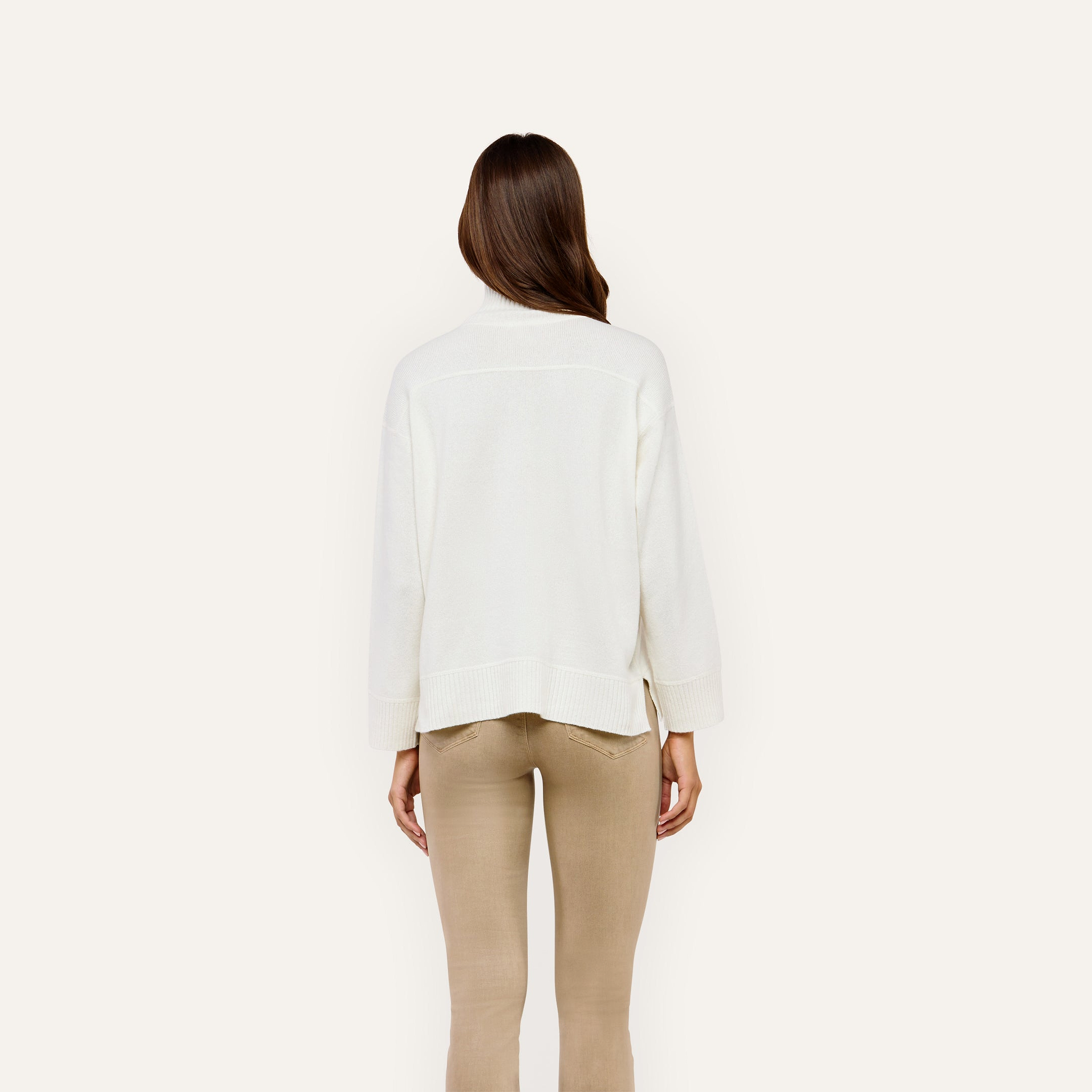 Back view of a person wearing a Selwyn Oversized Turtleneck in merino wool and tan pants.