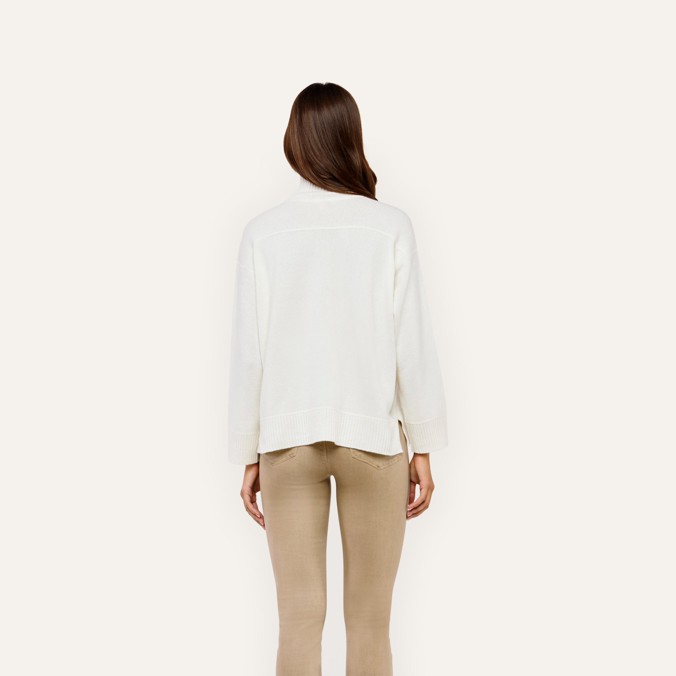 Back view of a person wearing a Selwyn Oversized Turtleneck in merino wool and tan pants.