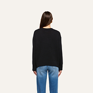 A person with long brown hair is seen from behind, wearing the Paxton Oversized Pullover and blue jeans against a plain, light background.