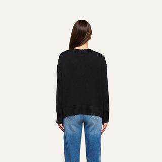 A person with long brown hair wears the Paxton Oversized Pullover in black and blue jeans, standing against a plain light background while facing away from the camera.