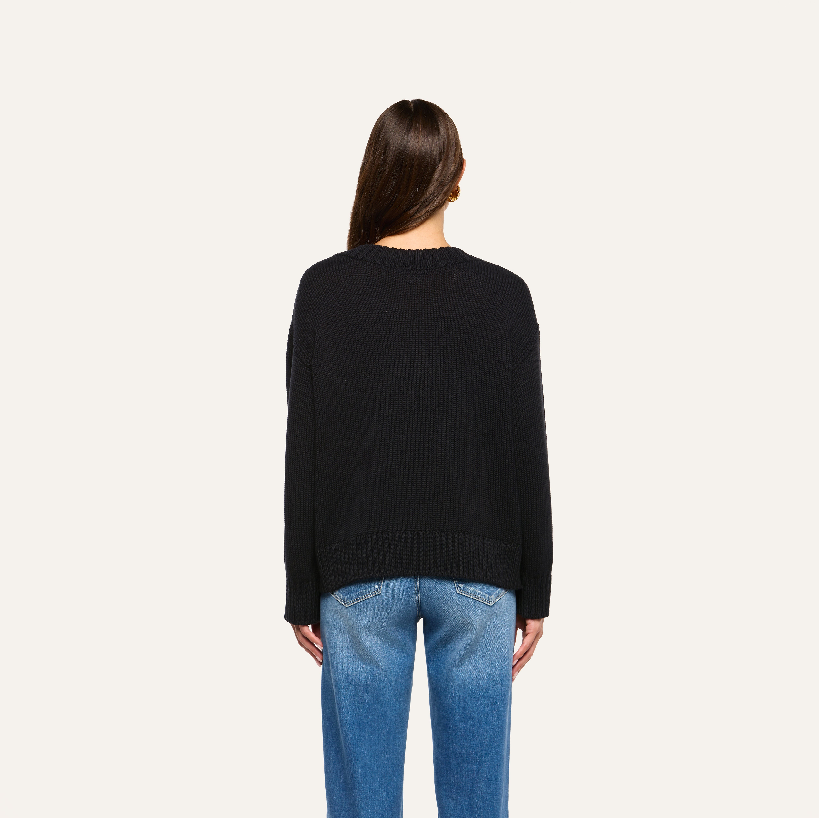 A person with long brown hair is seen from behind, wearing the Paxton Oversized Pullover and blue jeans against a plain, light background.