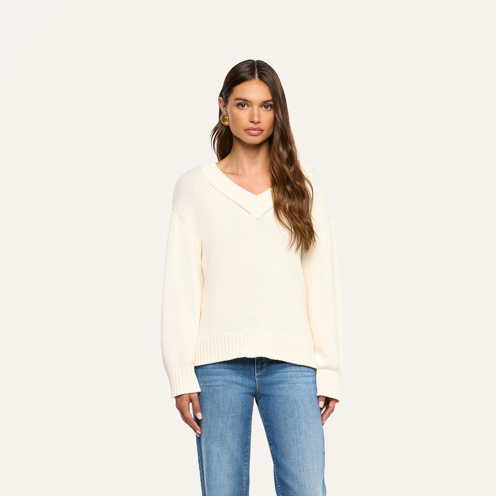 A woman wearing the Paxton Oversized Pullover in ivory and blue jeans stands facing forward against a plain, light background.