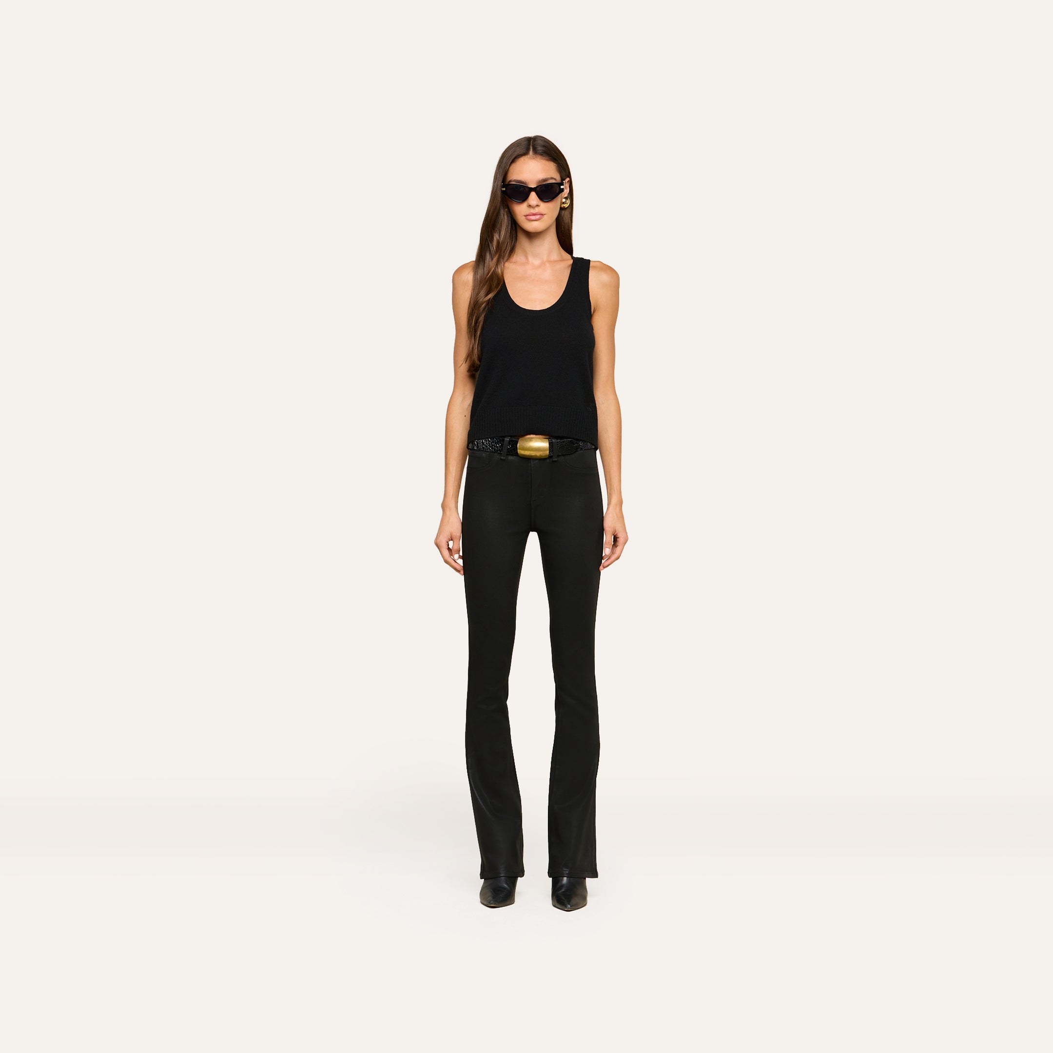A woman wearing sunglasses, the Filou Cashmere Tank in black, black pants, a belt with a gold buckle, and black shoes stands facing forward against a plain white background.