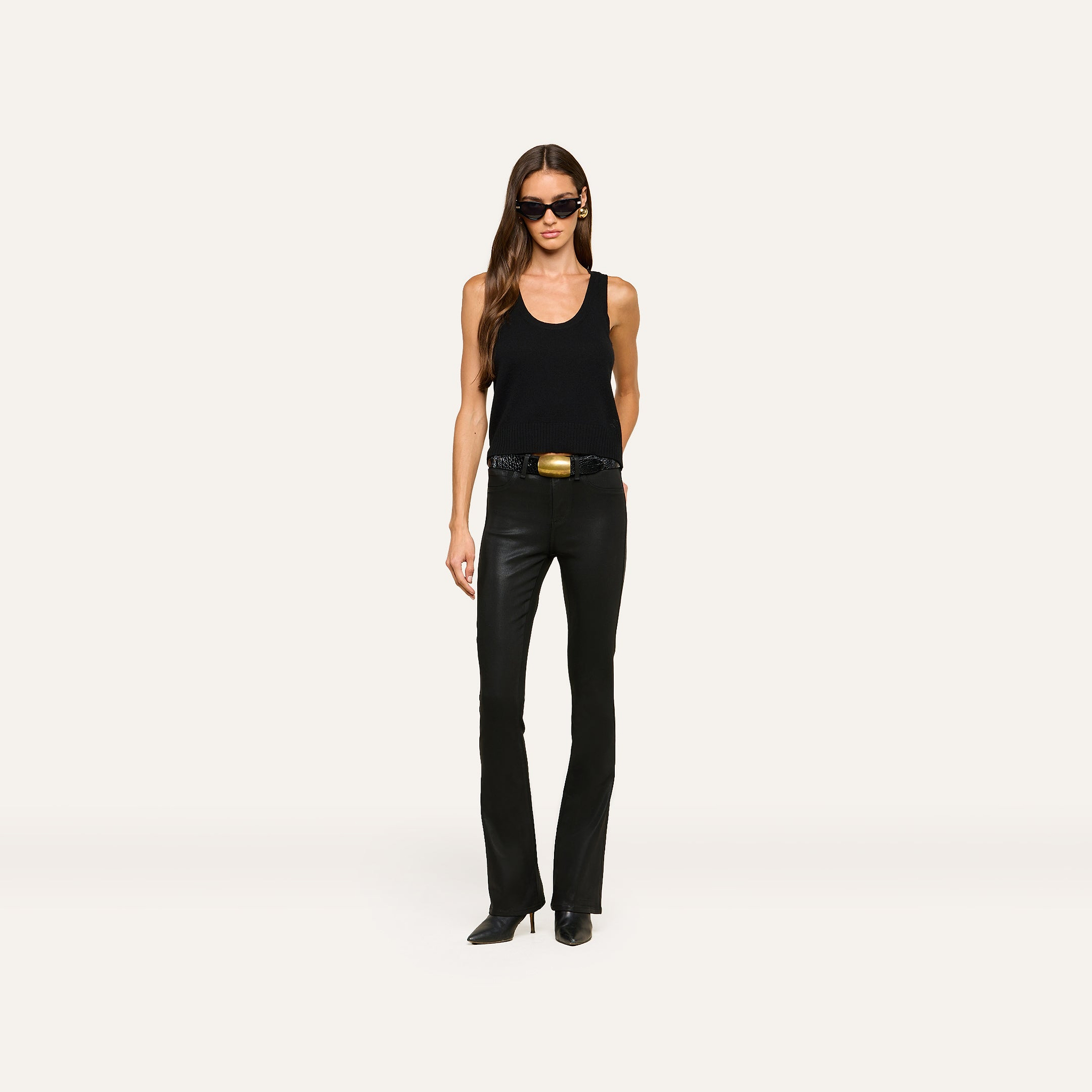 A woman wearing the Filou Cashmere Tank in black, paired with black leather pants, a black belt with a gold buckle, black pointed boots, and sunglasses stands against a plain white background.