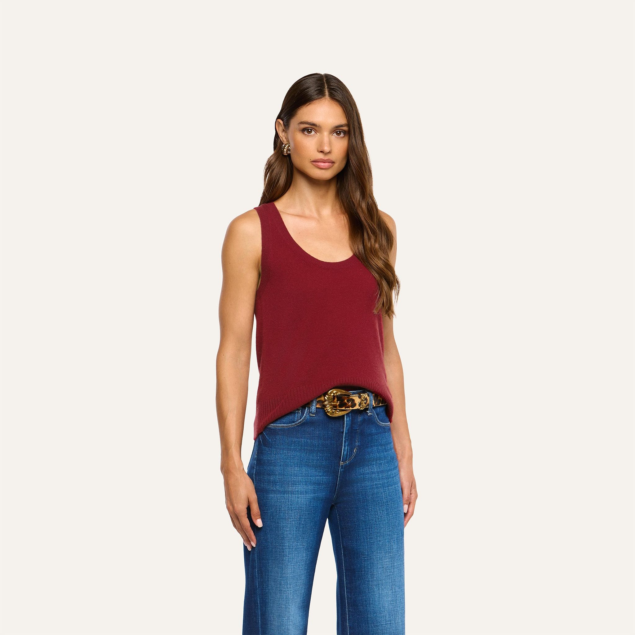 A person wearing a maroon Filou Cashmere Tank tucked into blue jeans with a gold-buckle belt.