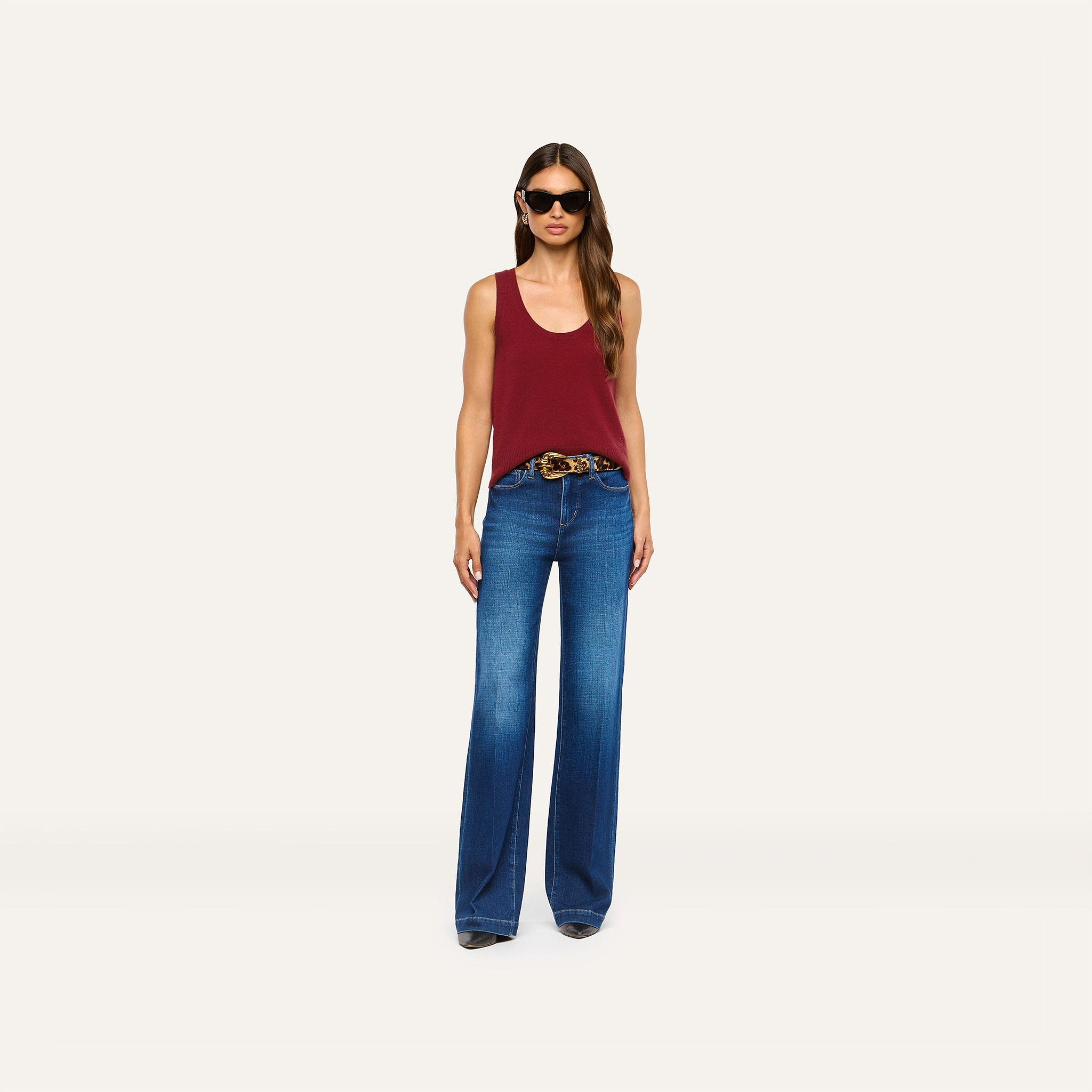 A person wears a maroon Filou Cashmere Tank tucked into wide-leg blue jeans with a leopard-print belt and black sunglasses.