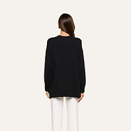 A person with long brown hair, facing away, is wearing a relaxed fit black Loden Tunic Pullover paired with white pants against a plain light background.