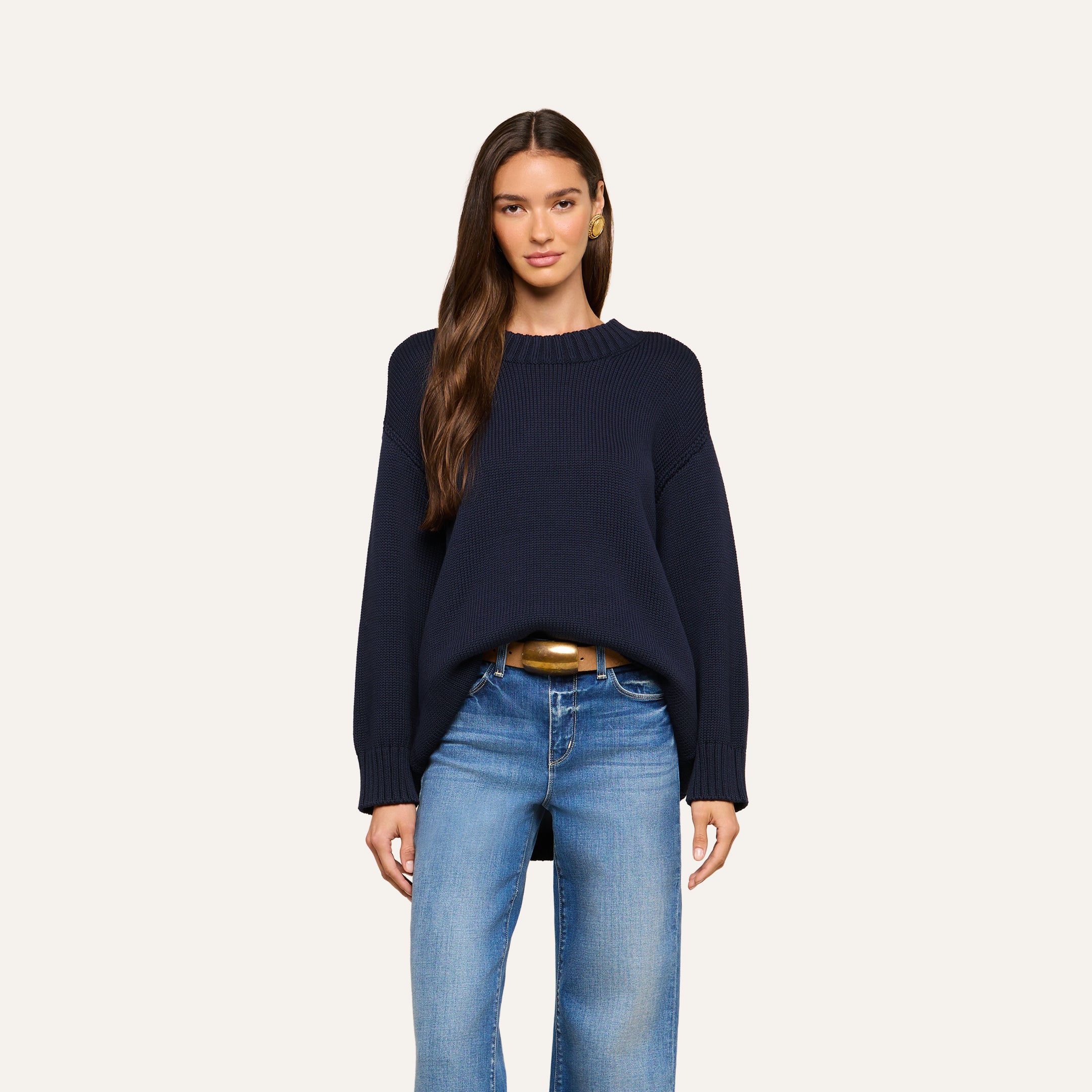 A woman is wearing the Loden Tunic Pullover in navy blue with blue jeans, standing and facing forward with a neutral expression against a plain light background.