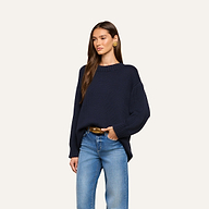 Woman wearing the Loden Tunic Pullover, a loose-fitting navy blue crewneck sweater, paired with light blue jeans and gold hoop earrings, standing against a plain light background.