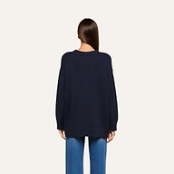 A person with straight brown hair is shown from behind, wearing a loose-fitting navy blue Loden Tunic Pullover and blue jeans against a plain light background.
