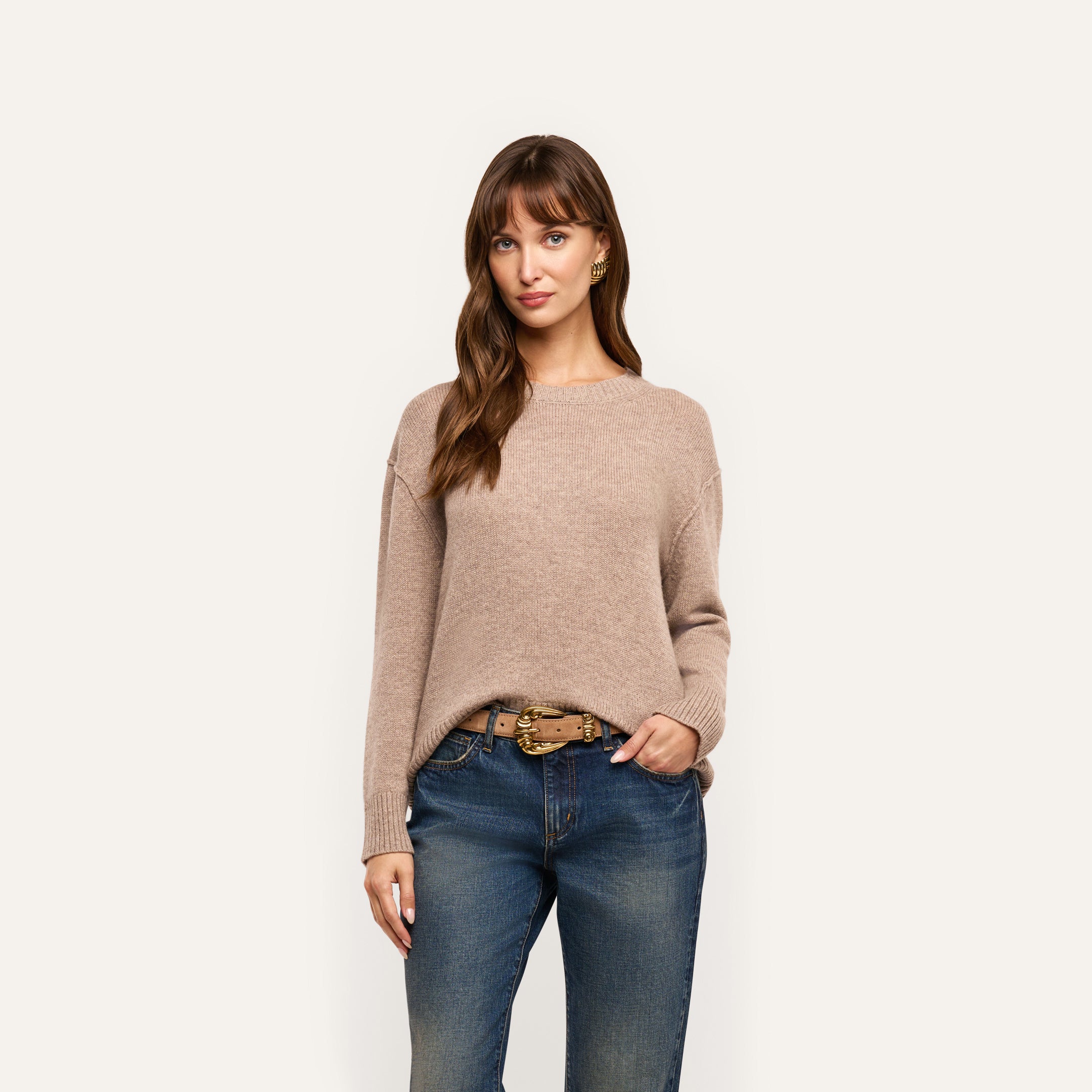A woman wearing a relaxed-fit, mid-weight Laine Cashmere Pullover tucked into blue jeans with a brown leather belt.